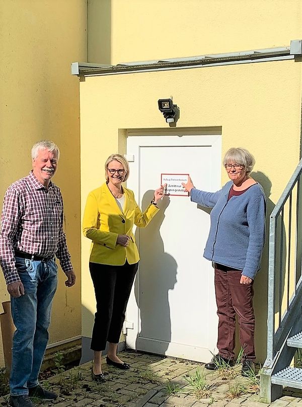 Alexander Fenker, Gertrud Nicola und Anja Karliczek vor dem Fahrstuhlschacht im Haus Apfelallee; der Fahrstuhl wurde mit Spenden aus der Arche-Wanderung 2019 finanziert
